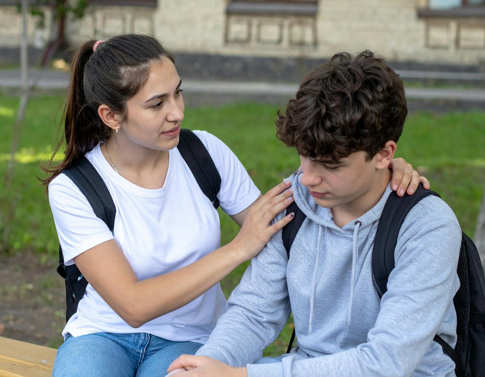 teen girl comforts sad friend outdoors at school
