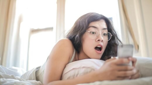 woman lying on bed holding smartphone
