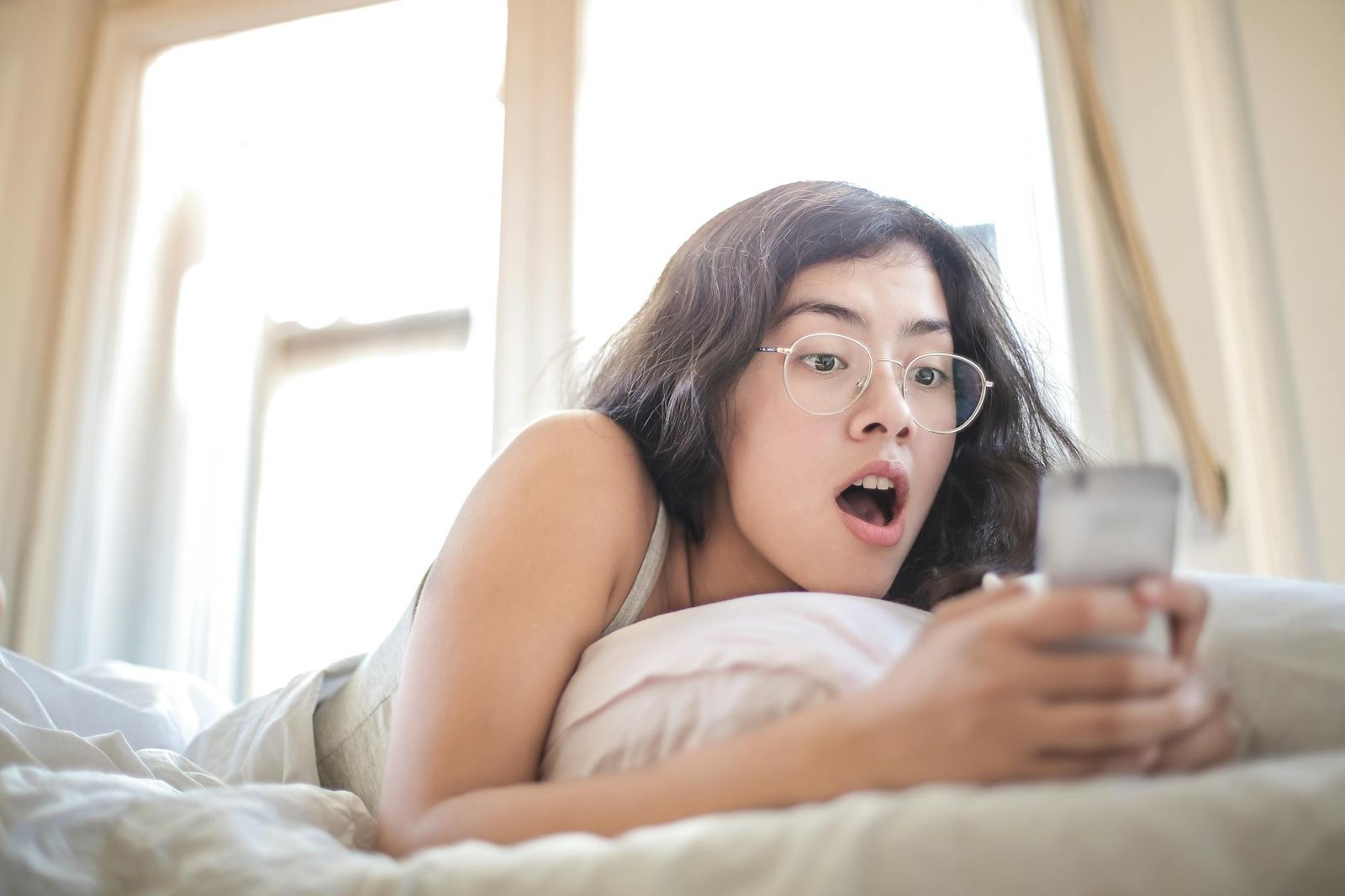 woman lying on bed holding smartphone