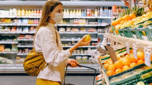 woman in yellow tshirt and beige jacket holding a fruit stand