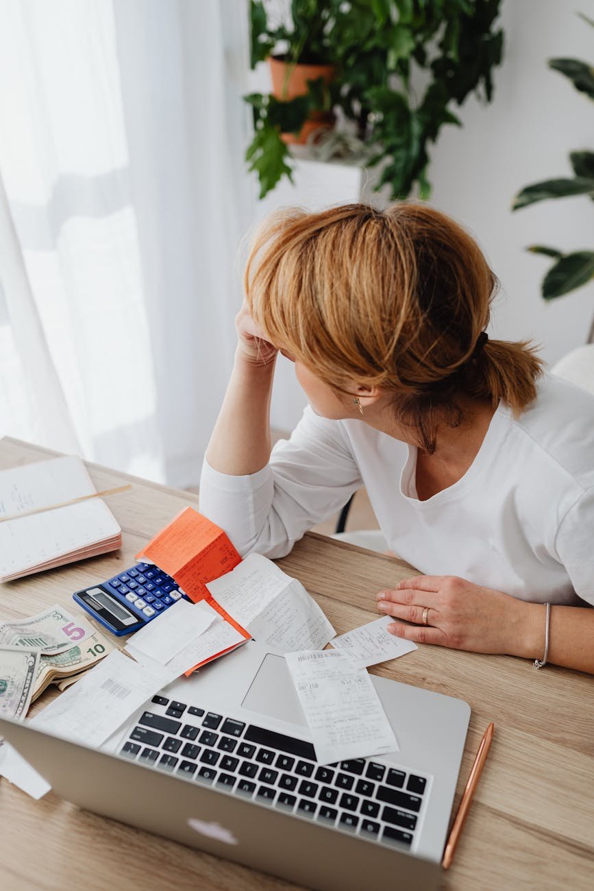 woman sitting next to a laptop with bills and monkey on the table