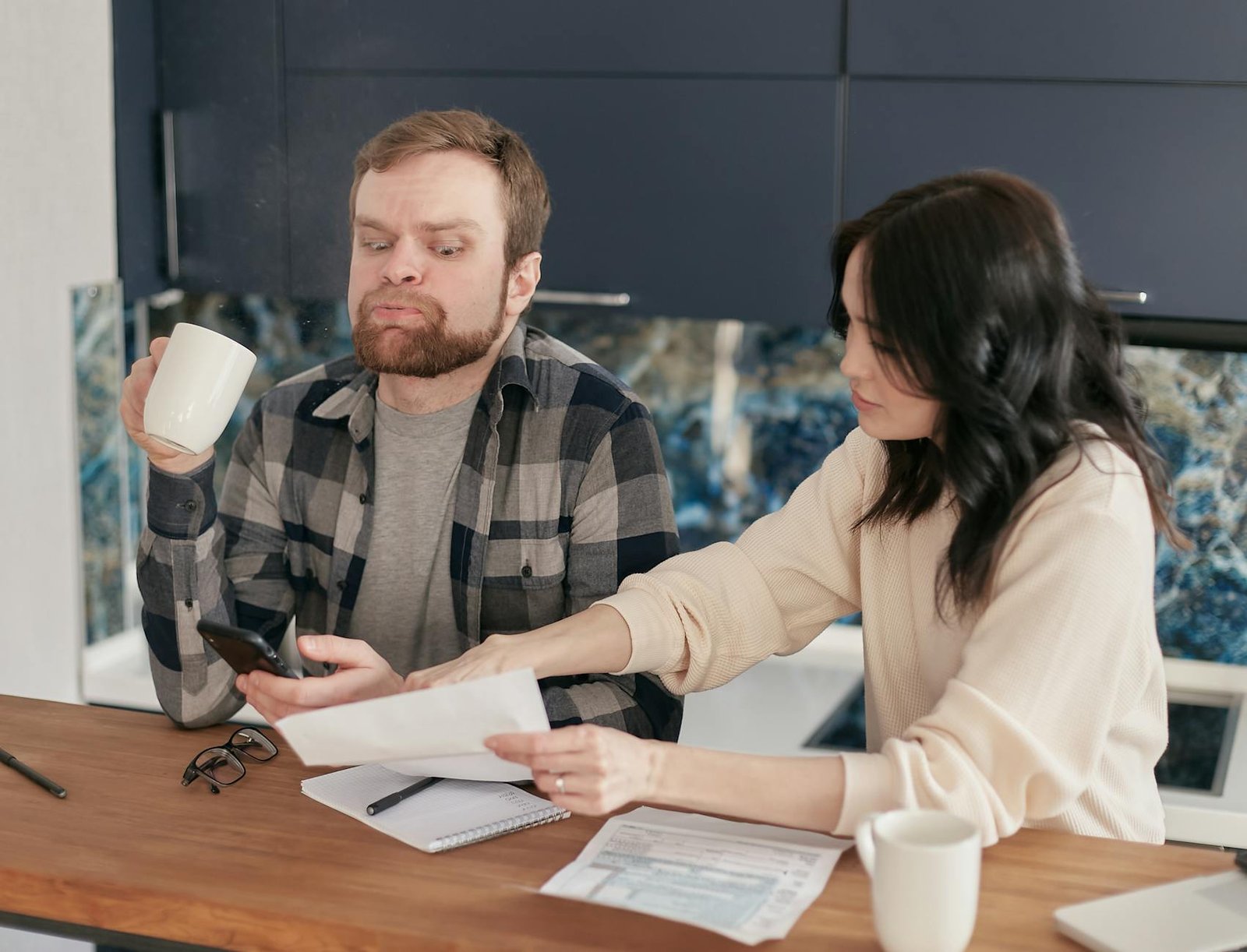 an anxious man holding a cup sitting beside a woman with a paper