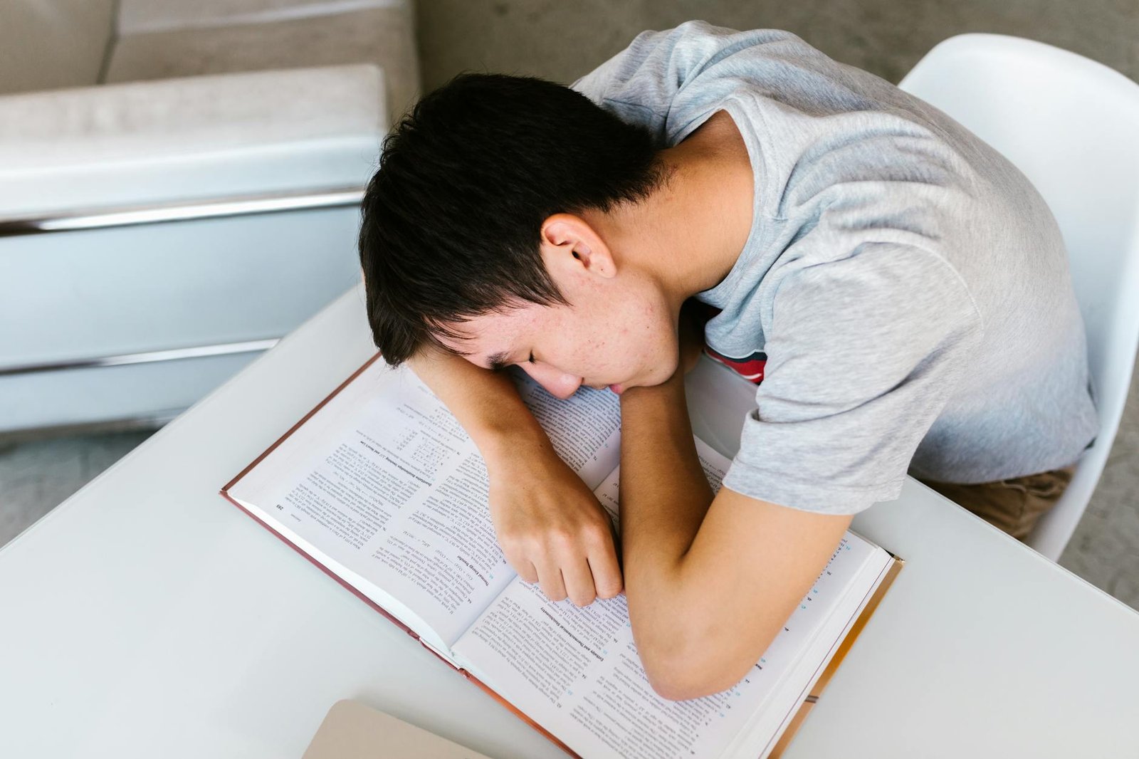 boy sleeping on an open book on a white table